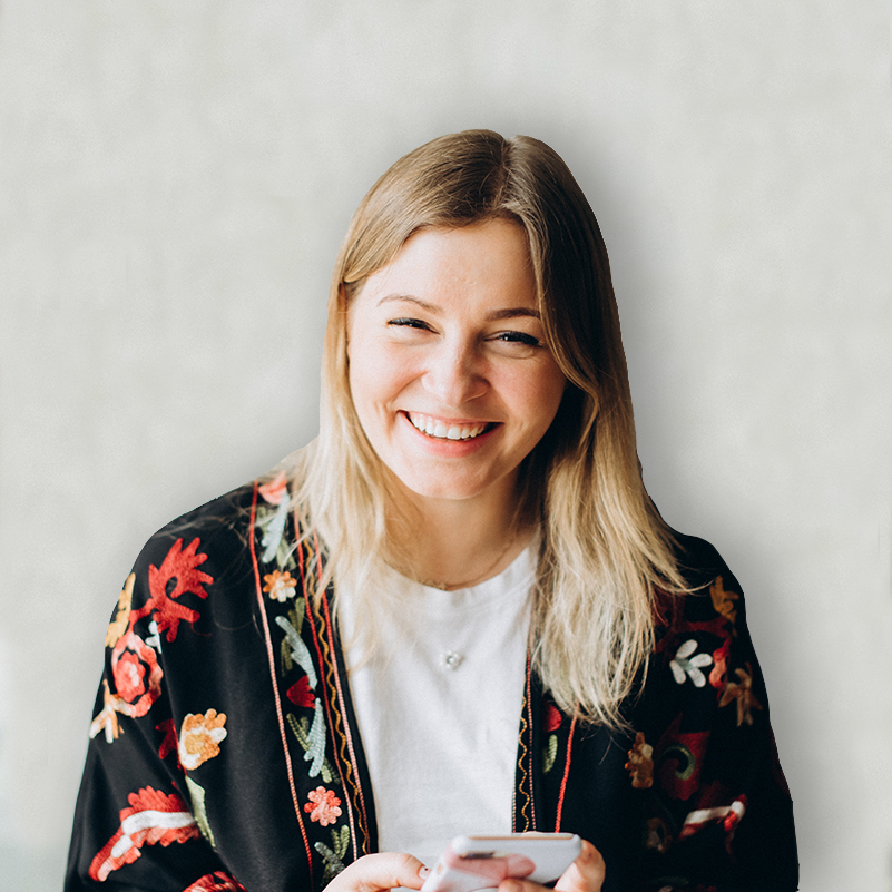 A cheerful person is wearing a floral black robe, holding a smartphone, with blonde hair, smiling against a white background.