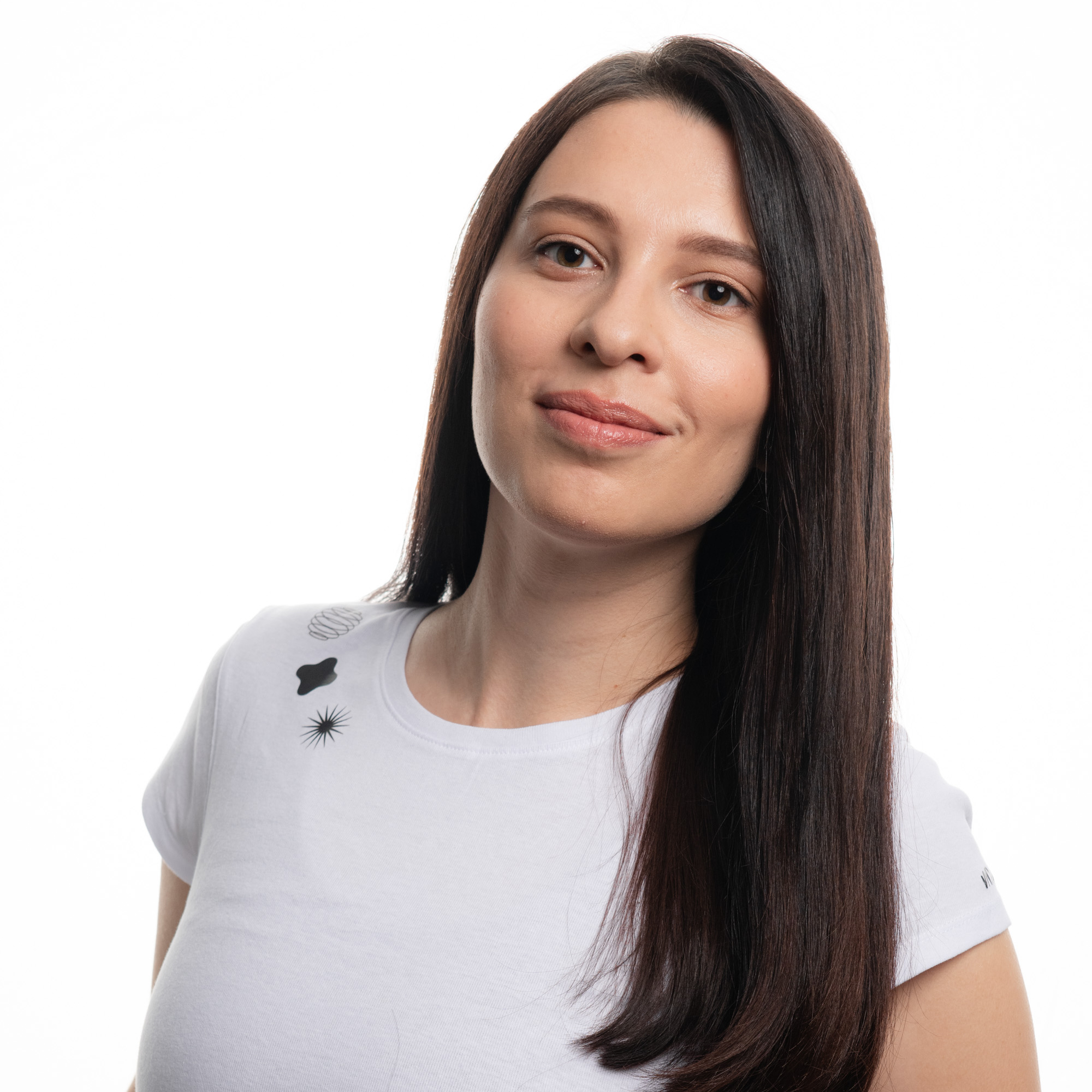 A person with long brown hair, wearing a white t-shirt with a subtle design, smiling subtly, against a white background.